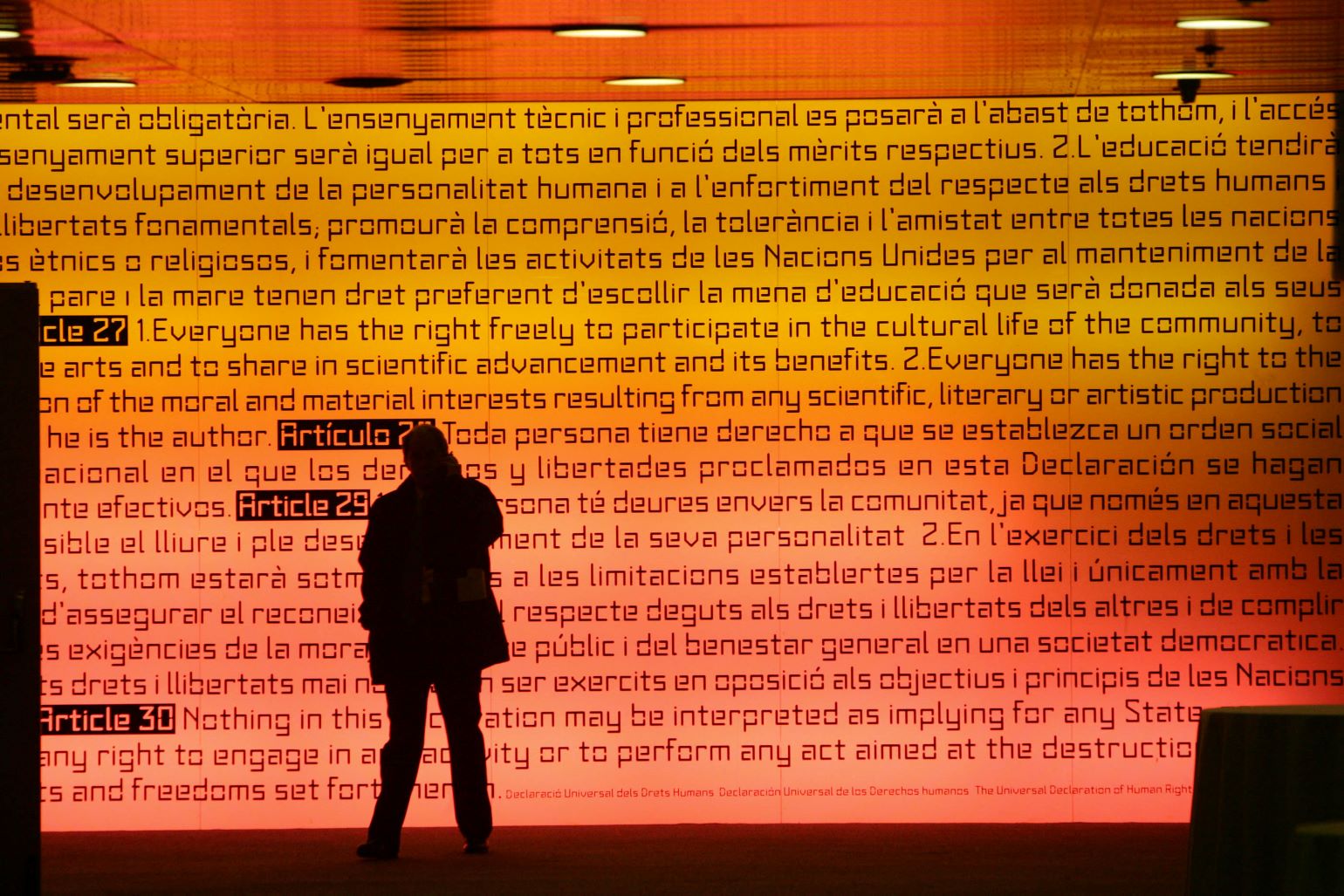 A man walks past an illuminated panel in bright orange light bearing the words of the last three articles of the Universal declaration of Human Rights in Spanish and English at the international convention centre in Barcelona on November 27, 2005. (Adrian Dennis/AFP via Getty Images)